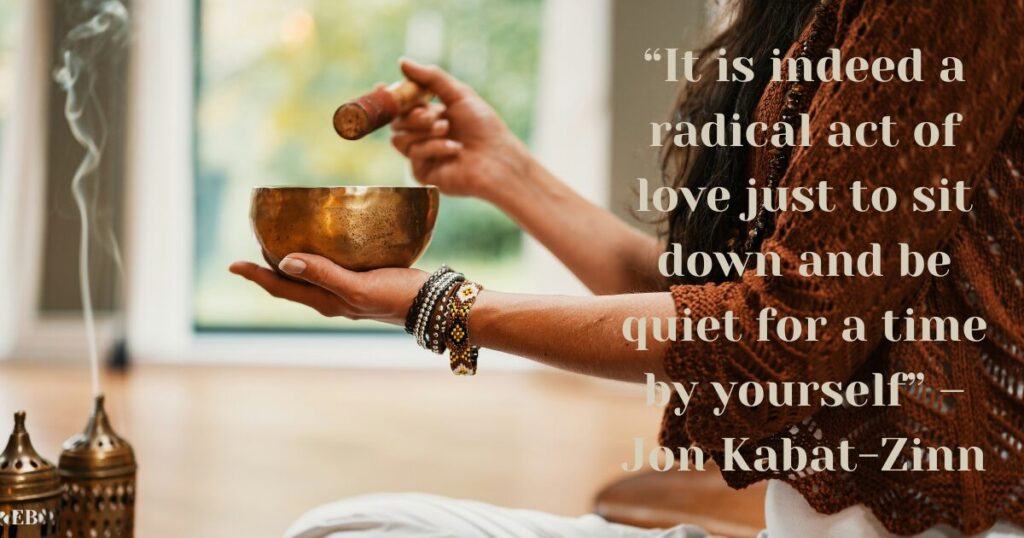 A woman sitting in cross-legged position with a singing bowl in her hand. Next to here the quote “It is indeed a radical act of love just to sit down and be quiet for a time by yourself” – Jon Kabat-Zinn