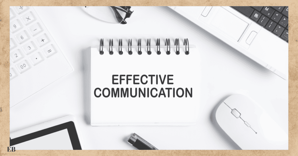 A spiral-bound notepad with the words "EFFECTIVE COMMUNICATION" sits on a white desk surrounded by a keyboard, a laptop, a computer mouse, a tablet, and a pen.